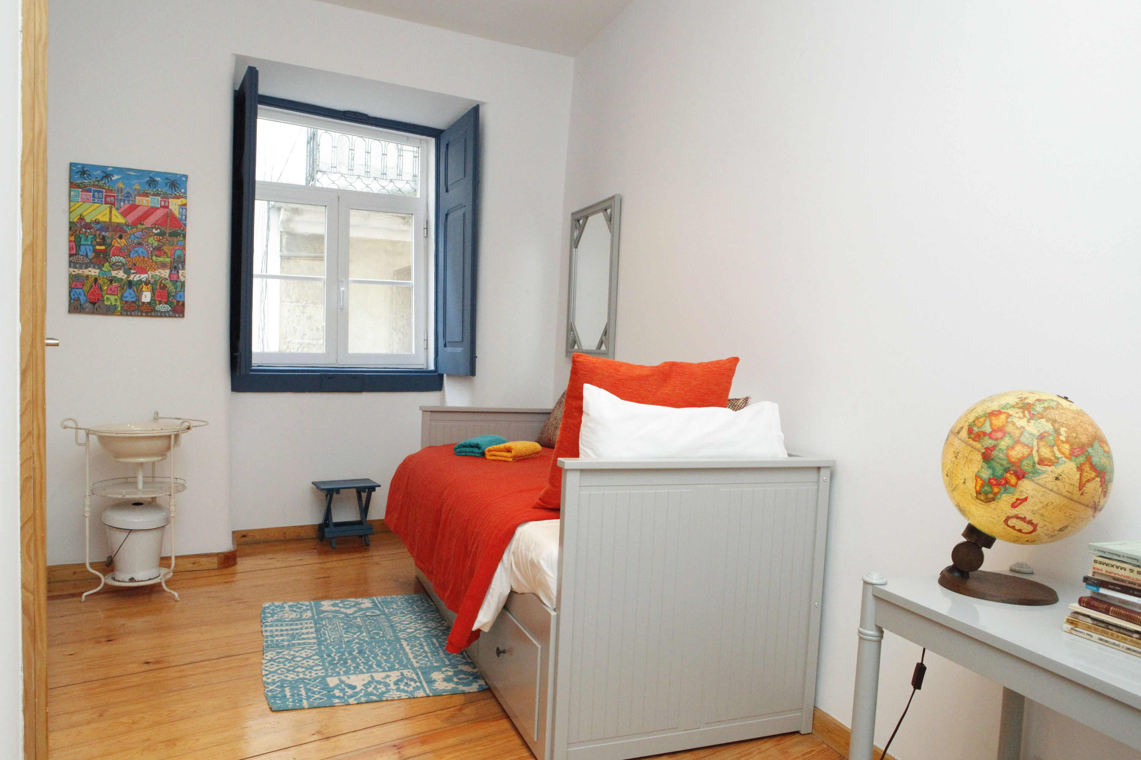 Een slaapkamer met een bed, een raam, een wereldbol en een kleine tafel.