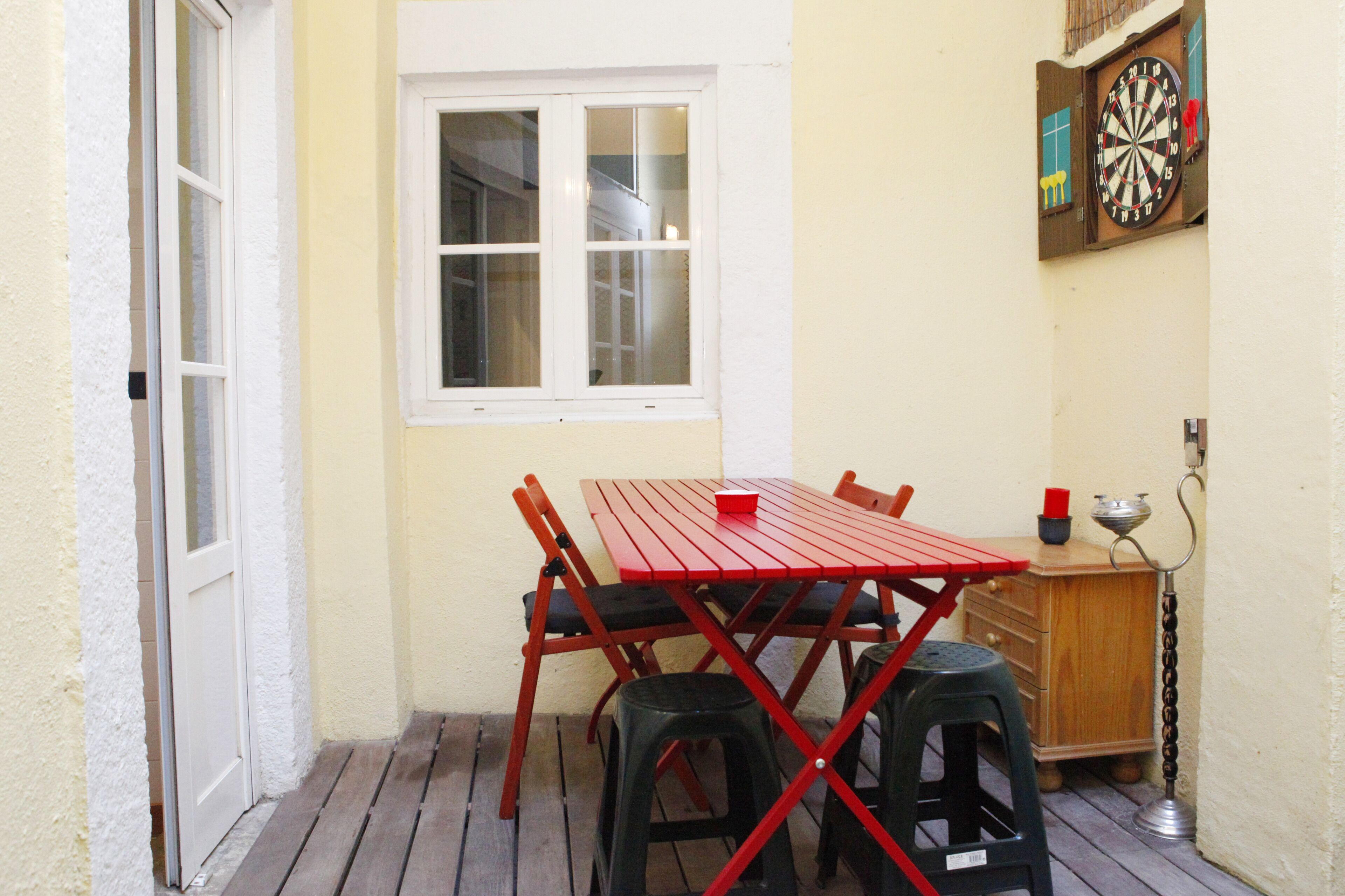 Un pequeño comedor con una mesa roja y sillas negras, una ventana y un dardo en la pared.