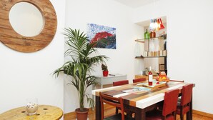 Un coin repas avec une table en bois, des chaises rouges, une plante en pot et un miroir au mur.