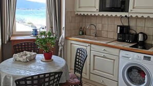 A compact kitchen with a washing machine, a coffee maker, and a view of the sea.