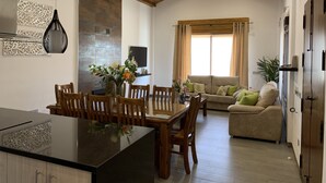 A spacious living area with a wooden ceiling, a dining table with chairs, a sofa, and a television.