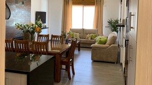 A spacious living area with a dining table and chairs, a sofa, and a kitchen area with cabinets and a countertop.