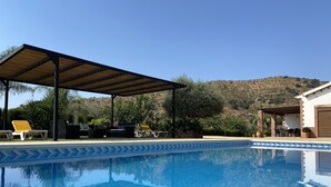 A pool area with a covered seating area and a view of a hilly landscape.