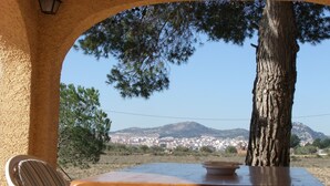 Una mesa de madera con sillas bajo un arco, con vistas a un pueblo y montañas.