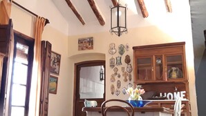 Comedor con vigas de madera, una araña y una pared decorada con diversos objetos.