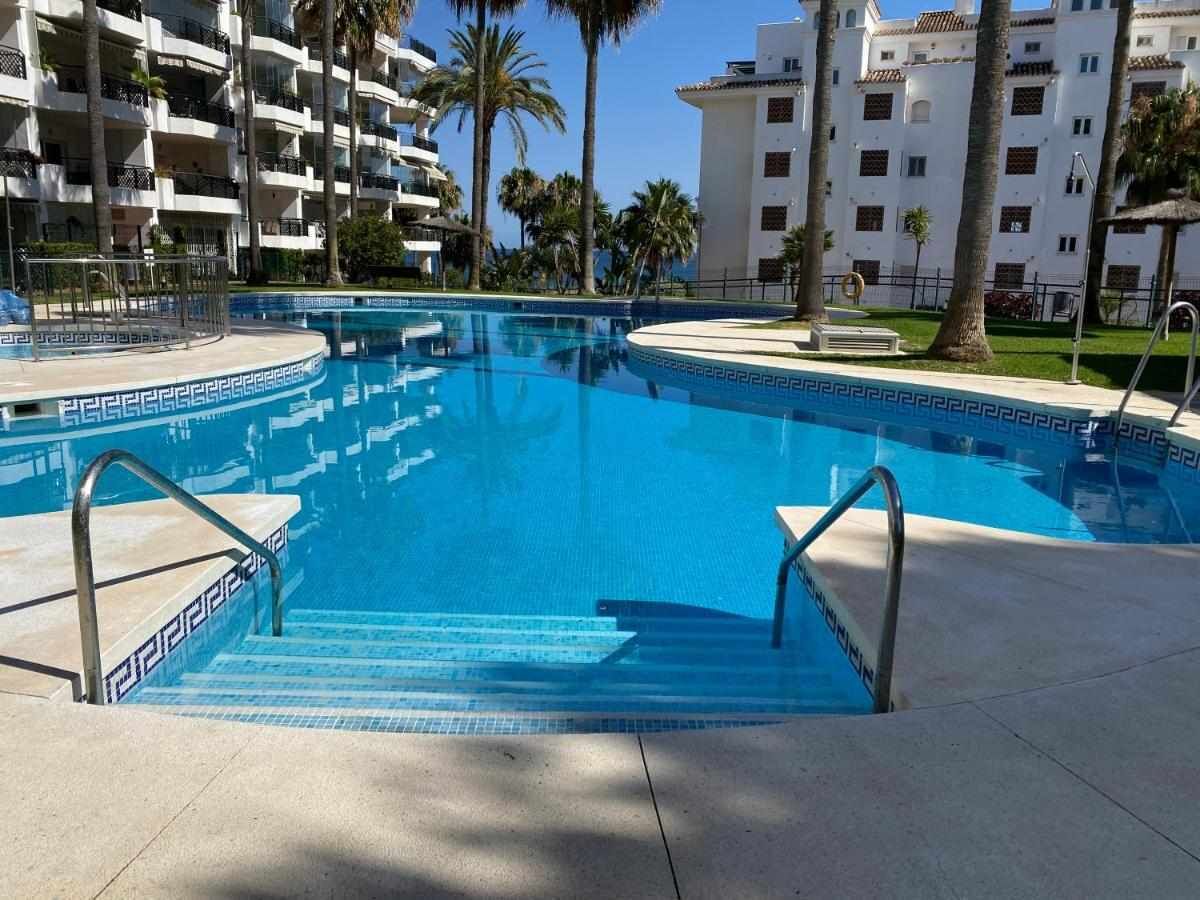 A swimming pool with steps leading into it, surrounded by a building with balconies and palm trees.