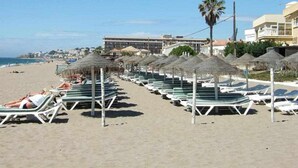 A beach with rows of sun loungers and thatched umbrellas, a clear sky, and buildings in the background. - Mi MI CAPRICHO LUXURY APARTMENT P.11 (Mijas)