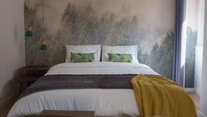 A bedroom with a bed, two pillows, a blanket, a small table, and a wall mural. - Ocean Center Apartments - Ocean Green (Cascais)