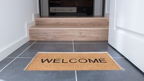 A welcome mat with the word "WELCOME" in a hallway leading to a staircase. - Ocean Center Apartments - Ocean Green (Cascais)