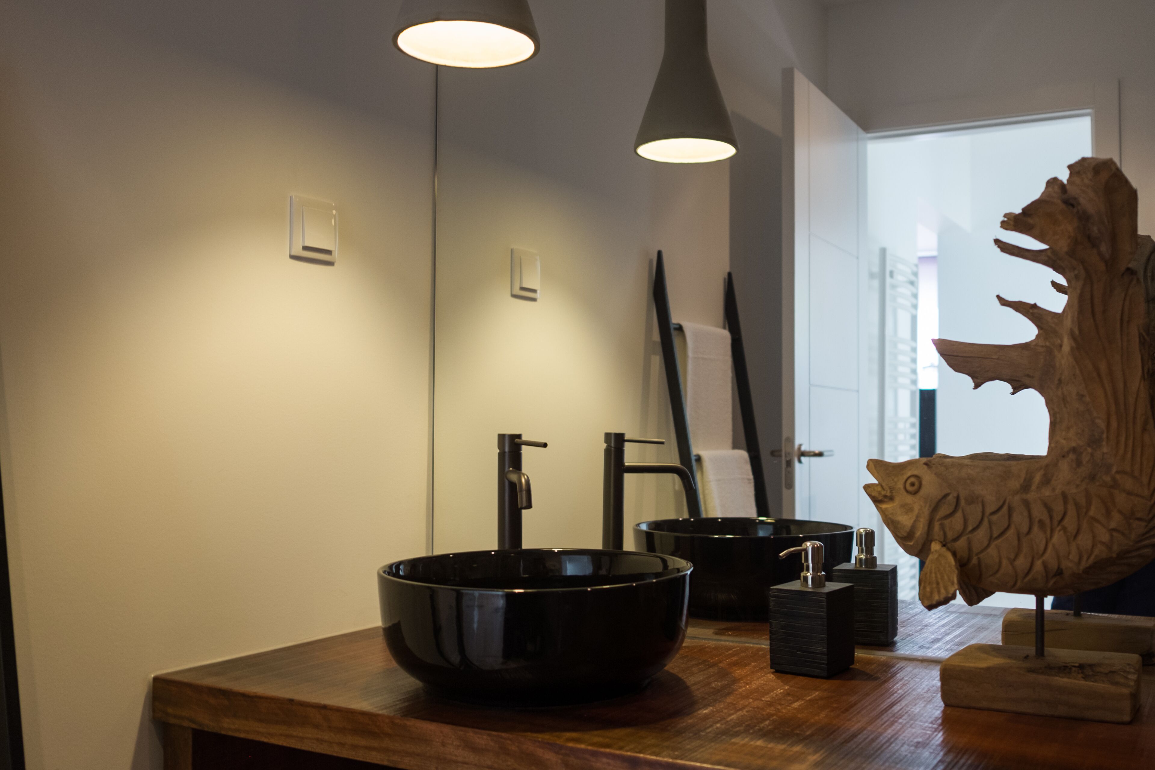 A modern bathroom with a wooden vanity, a black vessel sink, and a wooden fish sculpture.