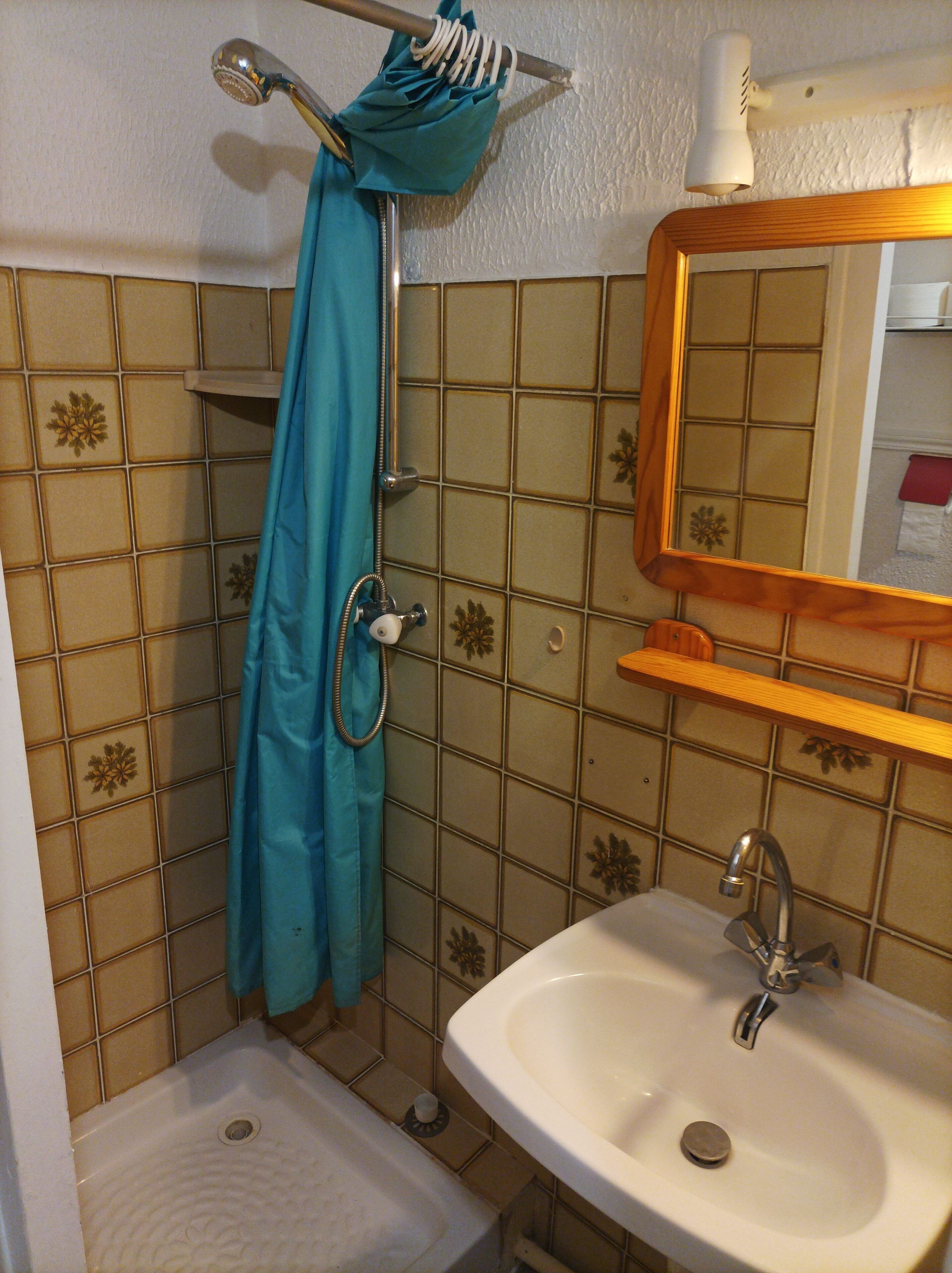 A bathroom with a sink, mirror, shower, and tiled walls.