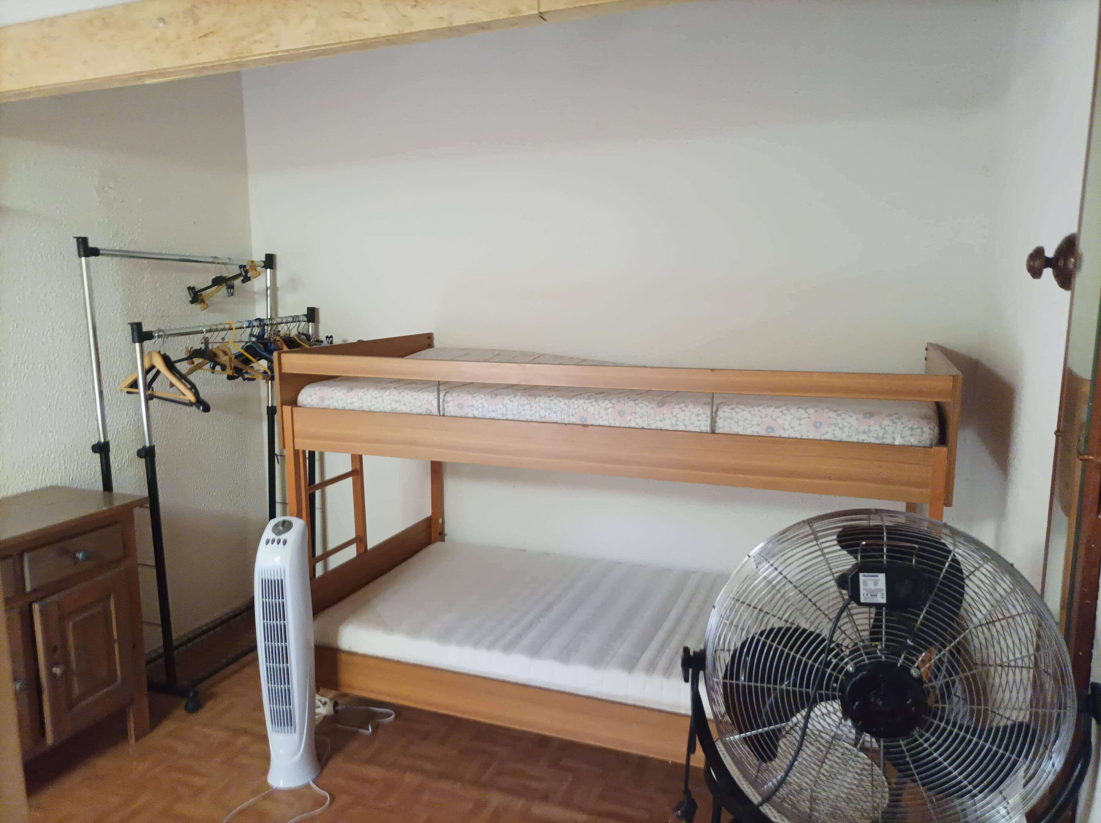 A bunk bed with a mattress and a fan, a wooden dresser, and a clothes drying rack.