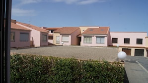 Una hilera de edificios rosados con techos de tejas rojas, un patio de grava y un seto en primer plano.