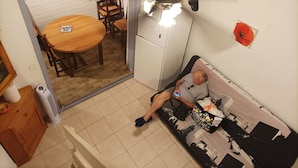Una habitación con una mesa de comedor, sillas, un sofá, un ventilador de techo, un refrigerador y una pared decorada con un cuadro.