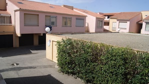 Una hilera de edificios rosados con tejados de azulejos, un camino de grava y un seto al frente.