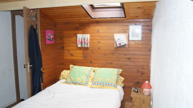Un dormitorio con techo de madera, una cama con almohadas estampadas, una mesita de noche con lámpara y un pequeño marco de fotos en la pared.