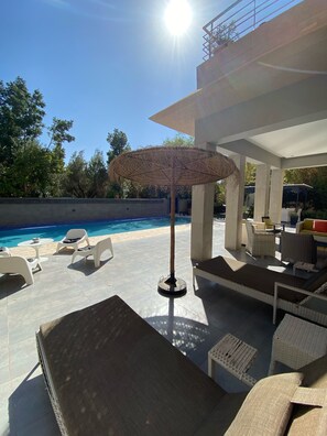 A poolside area with lounge chairs, a table, and a parasol.