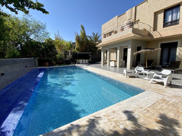 A swimming pool with lounge chairs and a covered seating area.