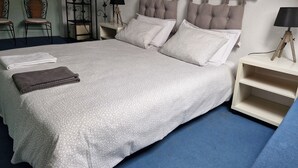 A neatly made bed with a patterned bedspread, two pillows, and two folded towels. There are bedside tables with lamps and a decorative metal partition. - 4-person gîte in farmhouse - heated indoor swimming pool  (Évellys)