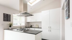 Une cuisine moderne avec des meubles blancs, un îlot central doté d’une cuisinière à gaz et une lucarne au-dessus.