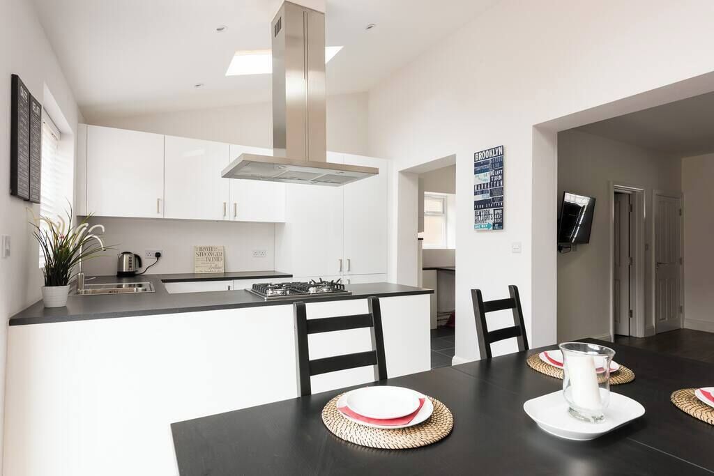 Una cocina moderna con armarios blancos, encimera negra y una isla central. Hay una mesa de comedor con individuales y una jarra de agua.