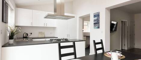 Una cocina moderna con armarios blancos, encimera negra y una isla central. Hay una mesa de comedor con individuales y una jarra de agua.