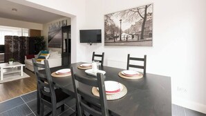 Un coin repas avec une table en bois foncé, dressée pour quatre personnes, entourée de chaises noires. Un téléviseur est fixé au mur, au-dessus de la table.