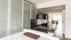 Une chambre d’hôtel moderne dotée d’un grand téléviseur à écran plat, d’une paroi en verre et offrant une vue sur l’espace repas.