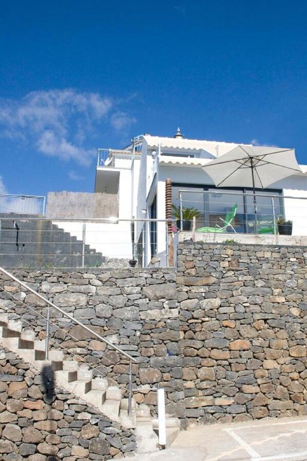 Un bâtiment moderne avec un escalier en pierre menant à une structure blanche surmontée d’un grand parasol.