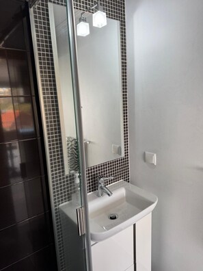 A bathroom with a glass shower enclosure, a white sink, and a mirror with black and white tiles. - House Crystal Calheta (Calheta (Madeira))
