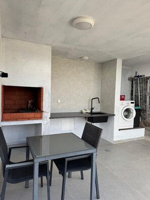 A compact kitchen with a built-in grill, a washing machine, and a dining area with a table and chairs. - House Crystal Calheta (Calheta (Madeira))
