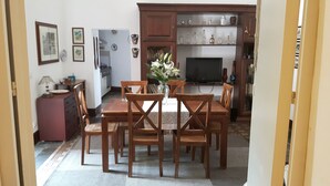 Un coin repas avec une table et des chaises en bois, un vase rempli de fleurs et, au fond, une cuisine.