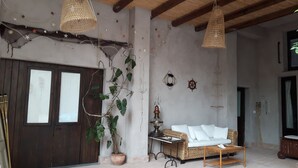 Un intérieur rustique avec une porte en bois, un canapé en osier, des lampes suspendues et une plante en pot.