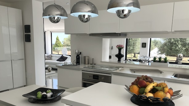 Une cuisine moderne avec des meubles blancs, un îlot central et des luminaires suspendus.