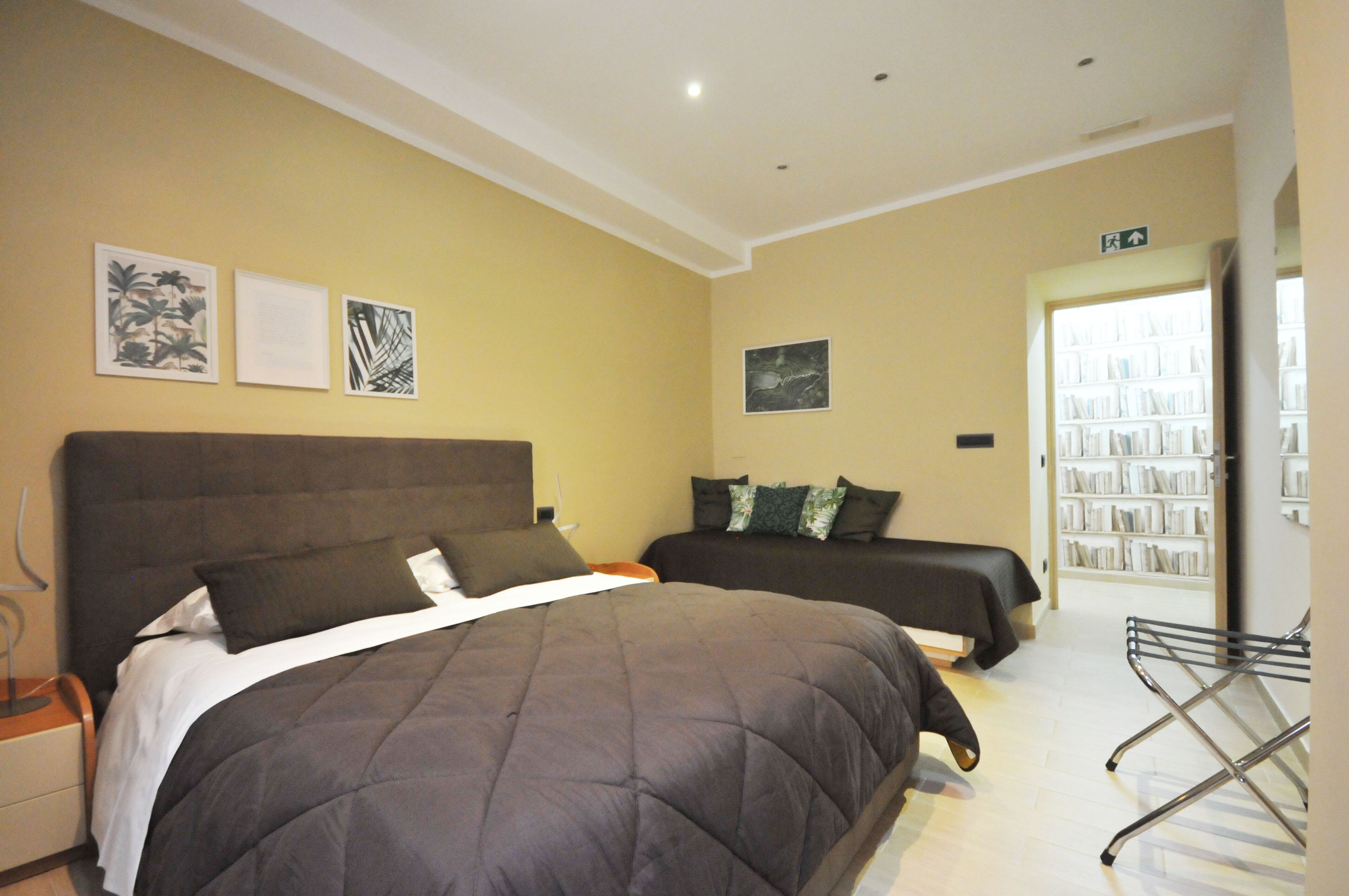A hotel room with two beds, a bookshelf, and a door leading to a hallway.