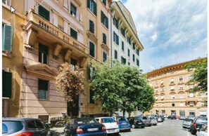 A street view of a row of multi-story buildings with parked cars and trees. - Next Stop St. Peter Rome (Rome)