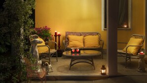 An outdoor seating area with wicker furniture, a glass table, and candles.
