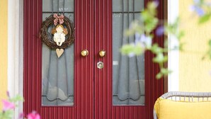 A red door with a wreath, two windows with curtains, and a yellow chair outside.