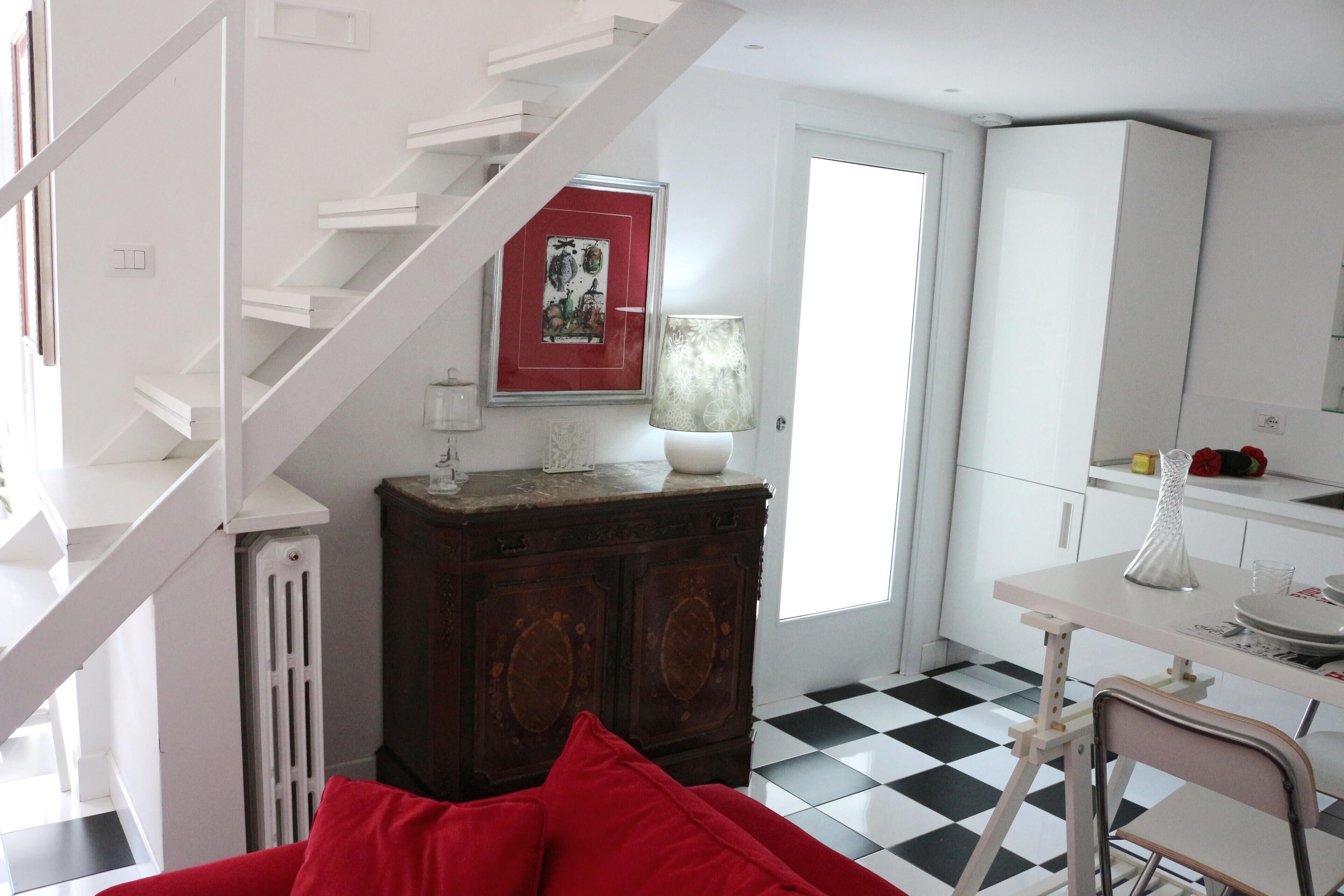 A room with a staircase, a dining table with chairs, a radiator, and a checkered floor.