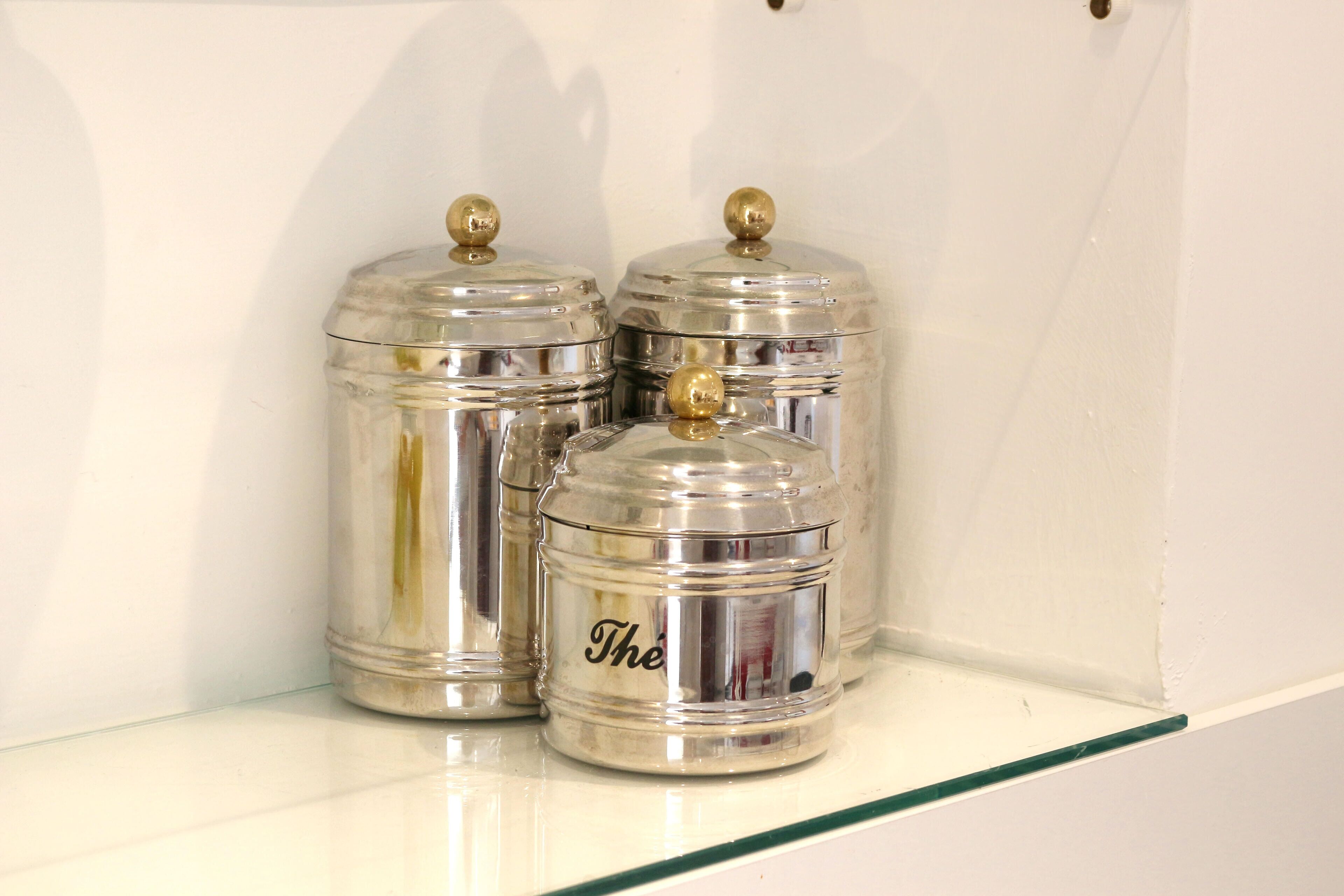 Tre contenitori metallici con coperchi su uno scaffale bianco.