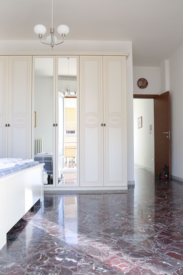 Un dormitorio con un armario grande, una cama con cabecero blanco y suelo de mármol.