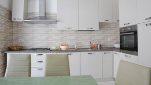 Une cuisine moderne avec des armoires blanches, une hotte de cuisinière en acier inoxydable et un coin repas agrémenté d’une nappe verte.
