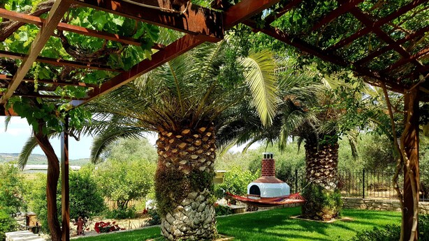 A garden with a stone-built outdoor oven, lush greenery, and a pergola structure. - Aloni Home,family holiday,relaxing and quiet place,private parking,garden (moires)
