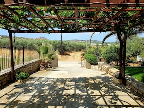 A covered outdoor area with a pergola, stone walls, and a dirt path leading to a gate.