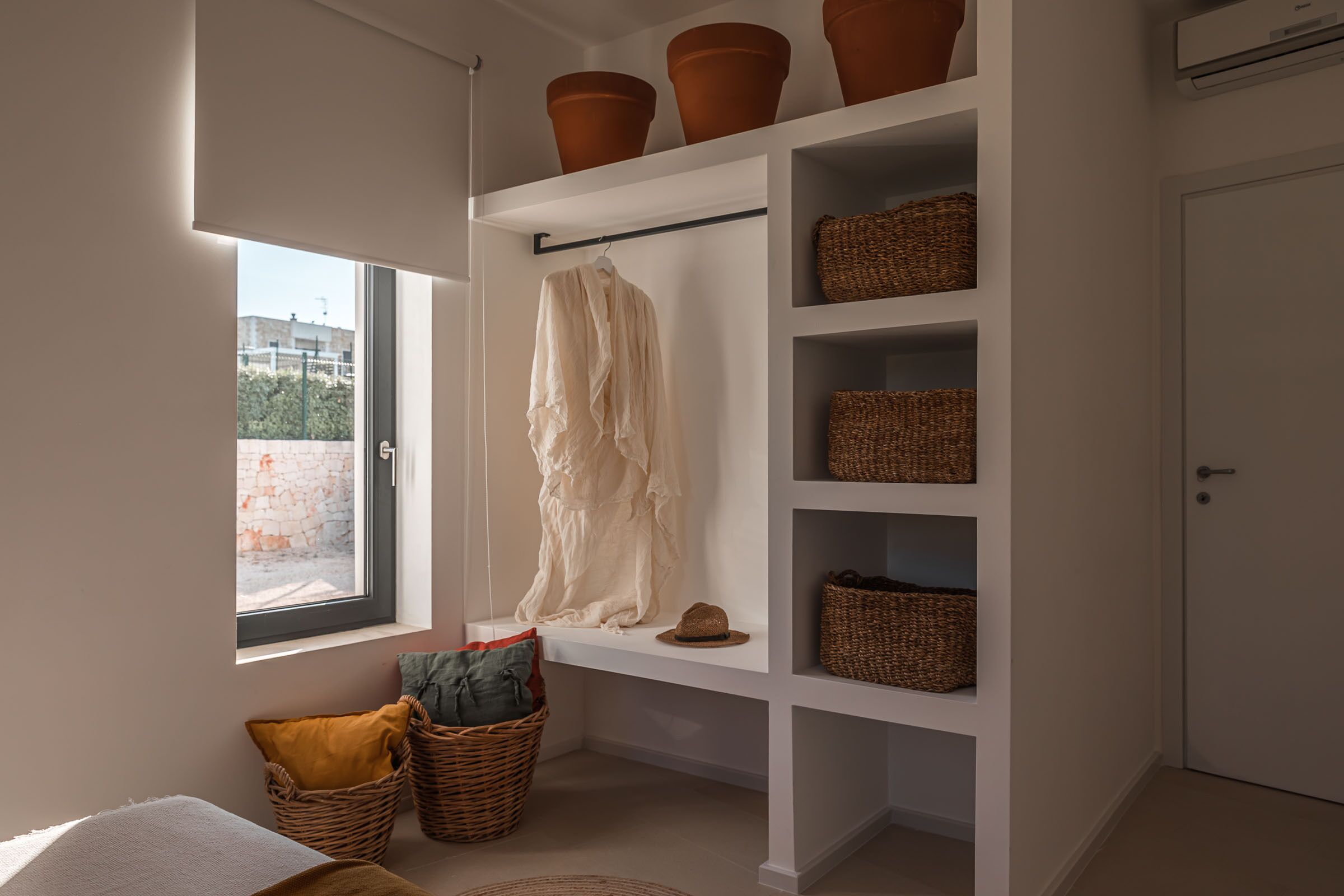 Ein Zimmer mit großem Fenster, einer weißen Bank mit Körben und einer Tür.