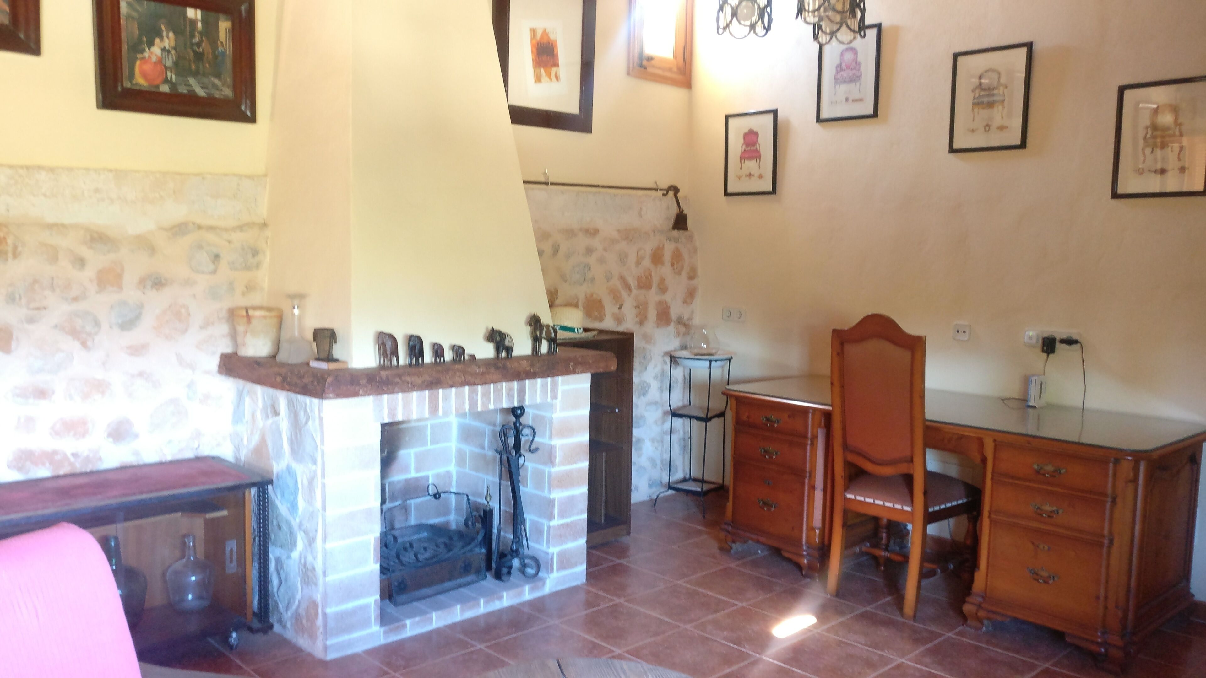 A room with a fireplace, a desk, a chair, and a stone wall.