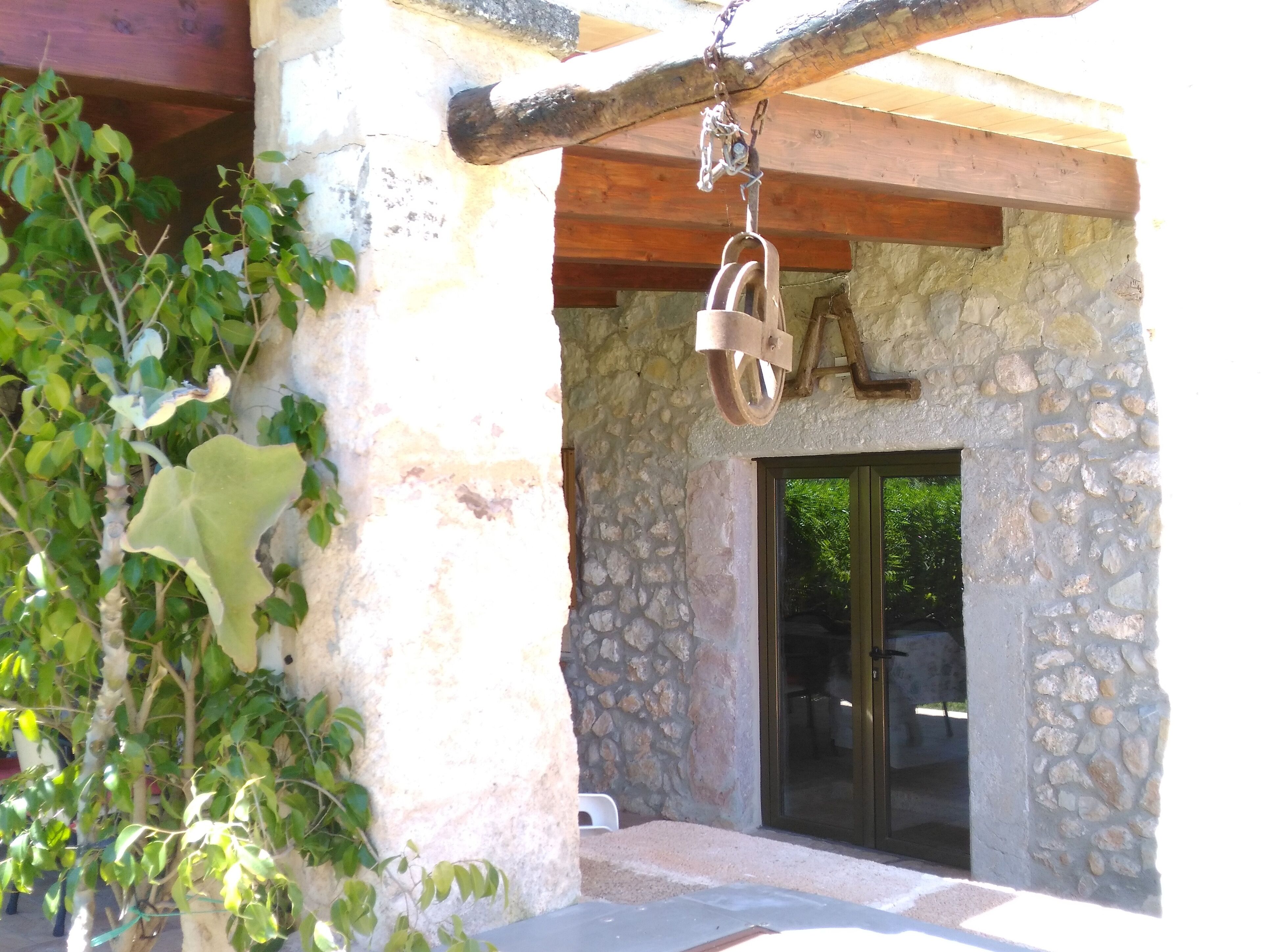 Un edificio de piedra con techo de vigas de madera, una campana colgante y un puerta de cristal.