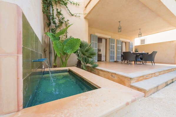 A pool area with a water feature, a dining table with chairs, and a covered seating area.