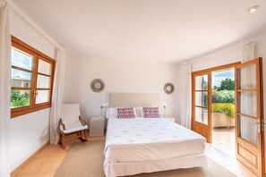 A bedroom with a bed, a chair, a nightstand, and a view of a garden through a sliding door.