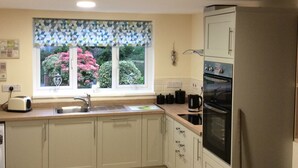 A kitchen with light-colored cabinets, a window with a geometric patterned blind, a sink, a toaster, a stove, and a trash bin.